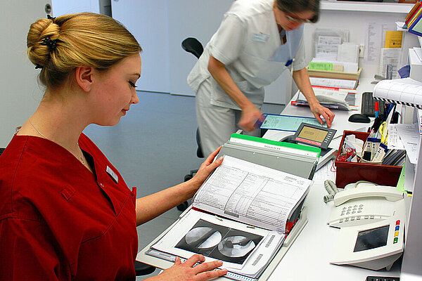 Zwei medizinische Fachkräfte arbeiten an einem Schreibtisch mit Dokumenten und Röntgenbildern