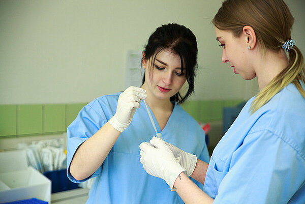 Zwei medizinische Fachkräfte in blauen Kitteln arbeiten mit einer Probe im Labor