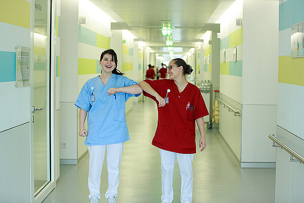 Zwei Pflegekräfte im Flur des Klinikums Landkreis Tuttlingen begrüßen sich mit einem Ellenbogengruß.