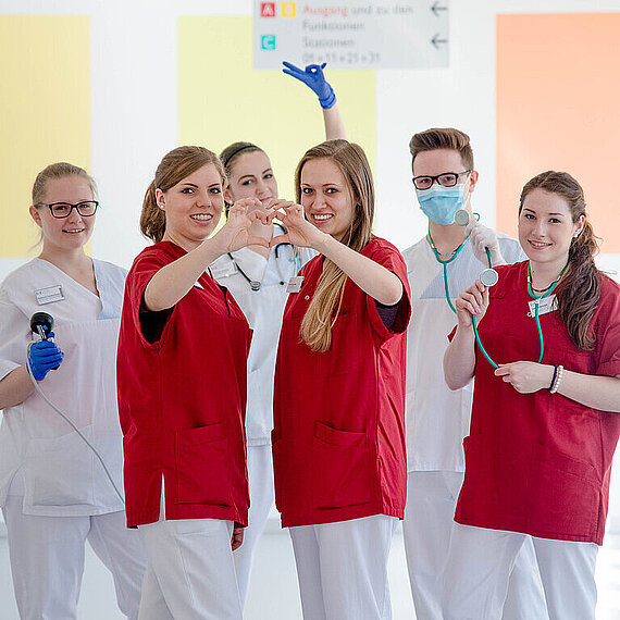 Junge Menschen im Klinikum, in Dienstkleidung, lächelnd vor einer bunten Wand Junge Menschen im Klinikum, in Dienstkleidung, lächelnd vor einer bunten Wand.